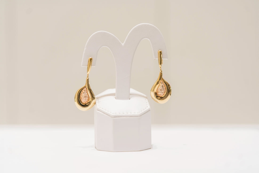 a pair of gold and diamond earrings on a white stand