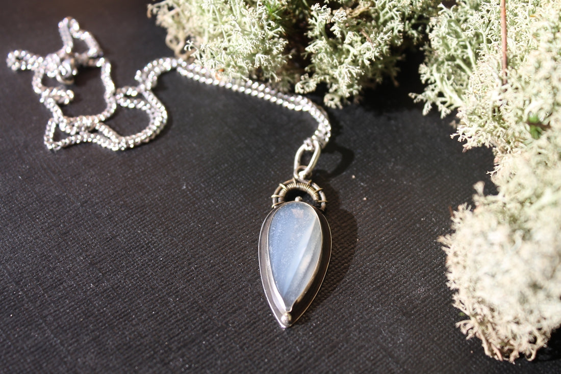 Silver necklace with a teardrop pendant on dark surface