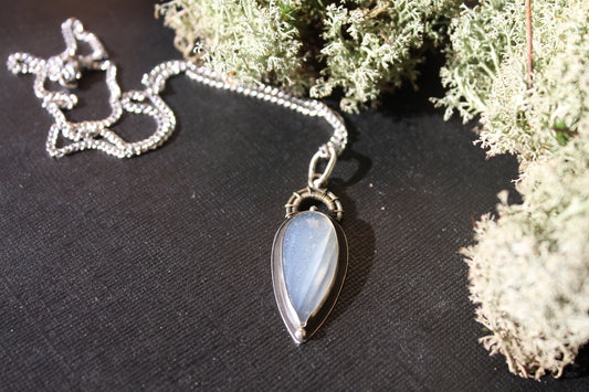 Silver necklace with a teardrop pendant on dark surface